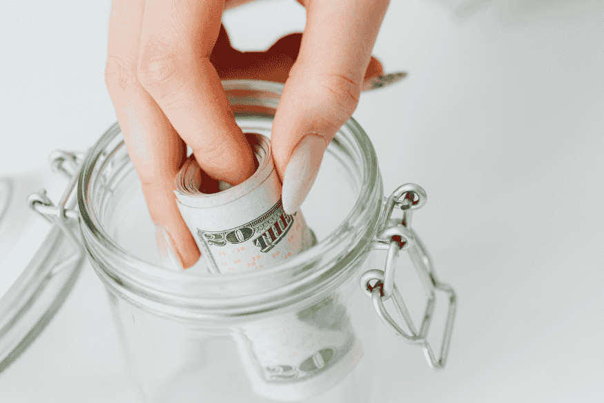 Hand putting rolled cash into a glass jar for effortless saving and automated money goals