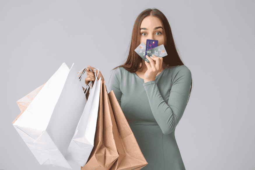 Woman holding shopping bags and credit cards, looking surprised or overwhelmed