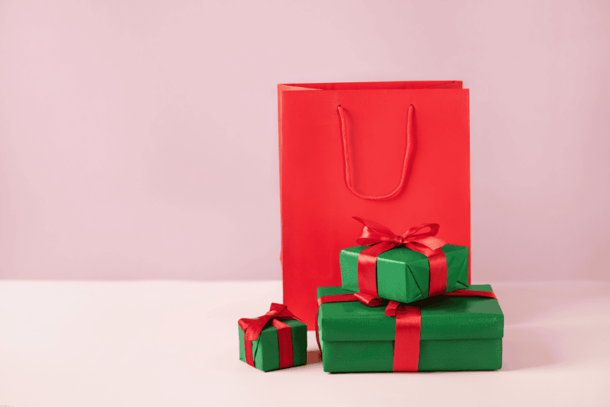 Red shopping bag and green gift boxes with red ribbons on a pink background