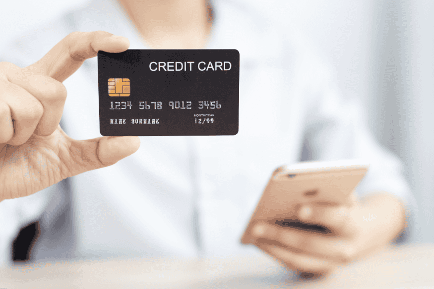 Person holding a black credit card while using a smartphone