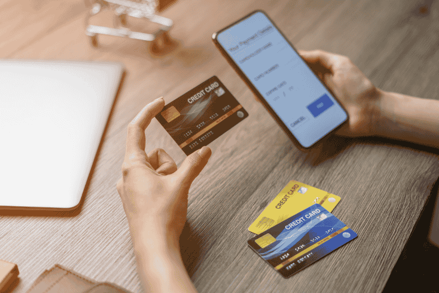 Person holding a credit card and smartphone while making an online payment, with more cards on the table.