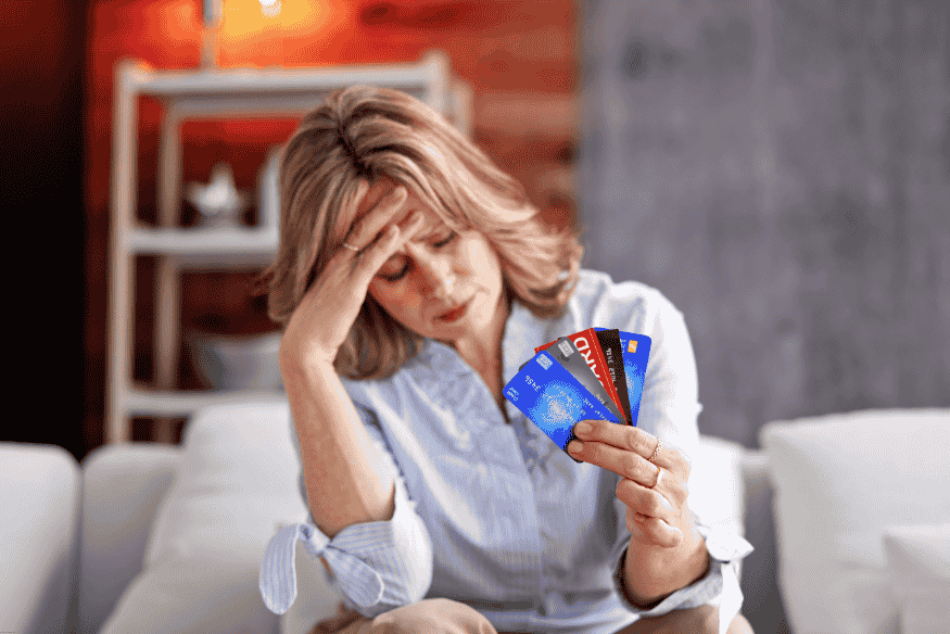 Stressed woman holding multiple credit cards while sitting on a couch
