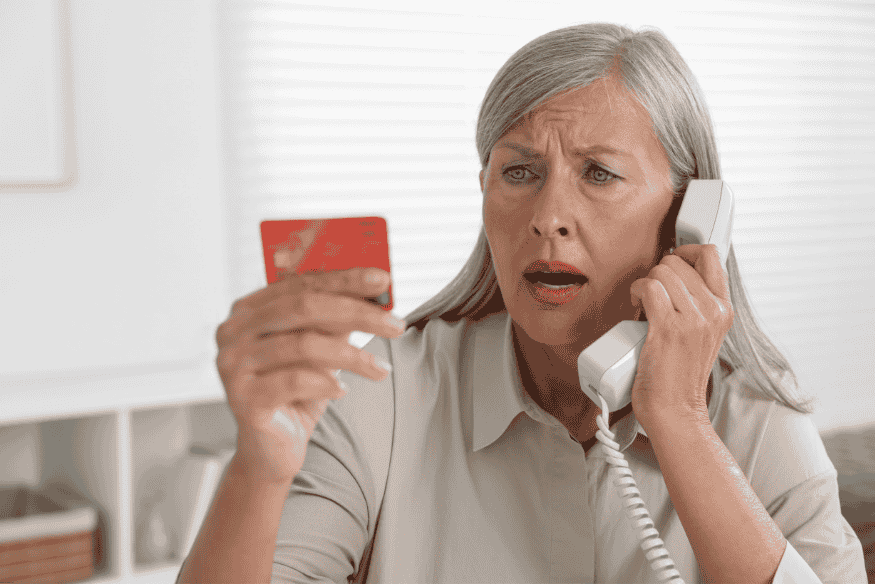 Worried senior woman calling support while holding a credit card.