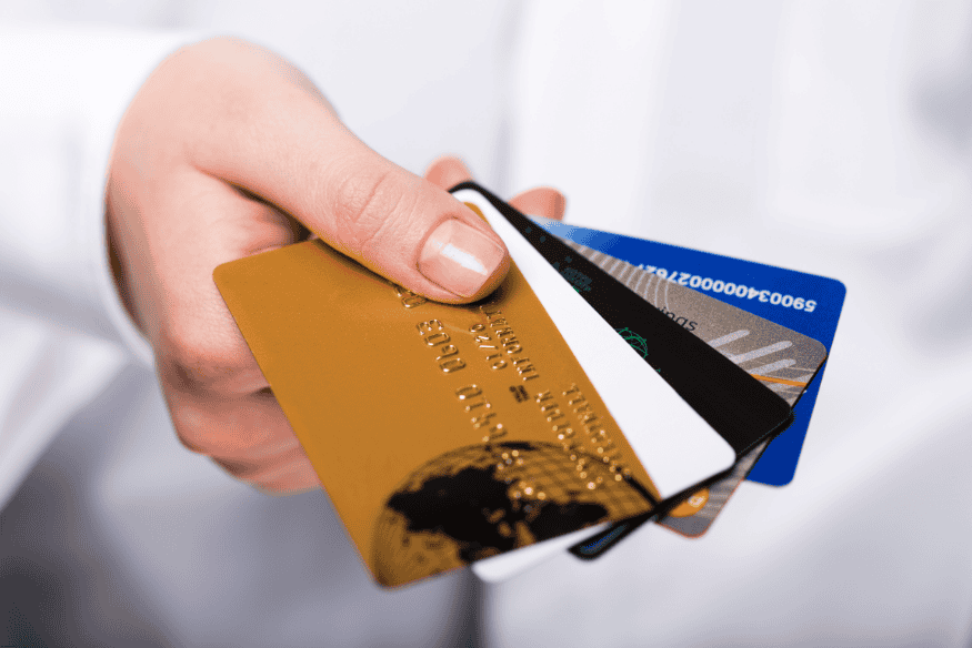 Hand holding several credit cards including gold, white, and blue cards