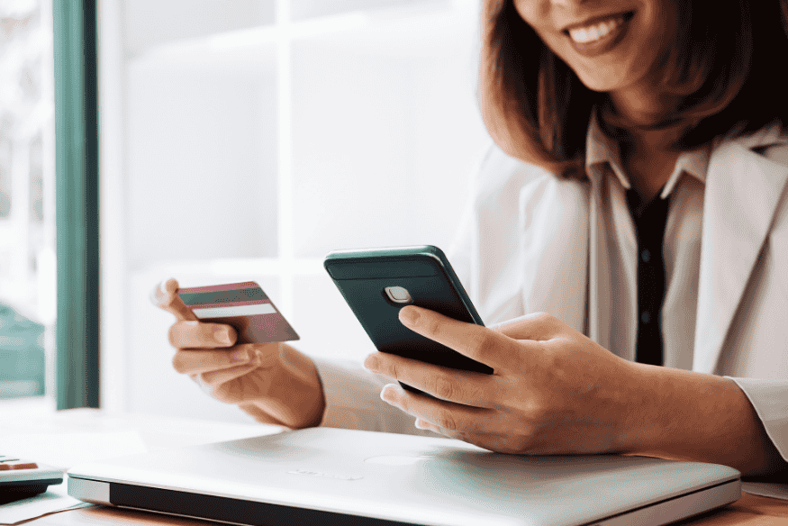 Smiling woman using a smartphone and holding a credit card, managing payments online.