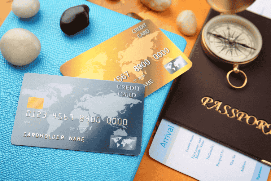 Travel-themed flat lay with credit cards, passport, compass, boarding pass, and pebbles